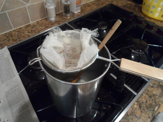Straining beeswax with cheesecloth on the cooktop.