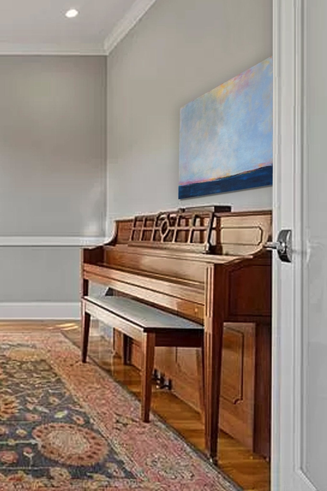 Blue seascape with low horizon and vast skies sits above a piano in the living room.